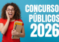 Jovem de cabelos cacheados, óculos e blusa vermelha segura livros com expressão surpresa diante de texto sobre concursos 2026