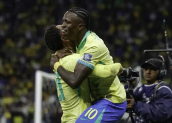 Vinicius Junior abraçando companheiro de seleção em comemoração de gol com camisa amarela da Seleção Brasileira em estádio lotado