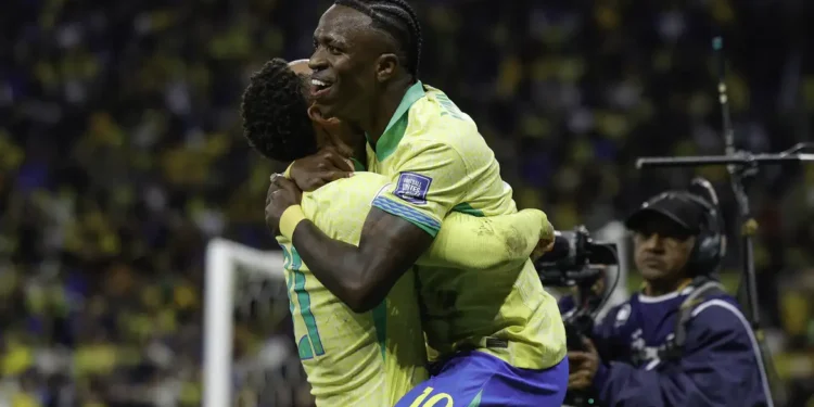 Vinicius Junior abraçando companheiro de seleção em comemoração de gol com camisa amarela da Seleção Brasileira em estádio lotado
