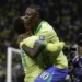 Vinicius Junior abraçando companheiro de seleção em comemoração de gol com camisa amarela da Seleção Brasileira em estádio lotado