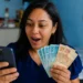 Mulher segurando dinheiro enquanto consulta informações no celular, representando o pagamento residual do FGTS.