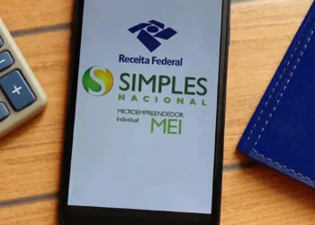 Tela de celular exibe logos da Receita Federal e do Simples Nacional para Microempreendedor Individual ao lado de calculadora cinza sobre mesa de madeira.