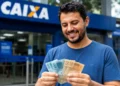 Homem segurando cédulas em frente a agência da Caixa, representando a confirmação de depósitos de até R$ 1.078,01 para CPFs finais 0 a 9.
