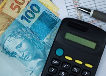 Cédulas de R$ 50 e R$ 100 ao lado de calculadora preta sobre planilha financeira, em referência à renegociação de dívidas pelo Novo Desenrola Brasil