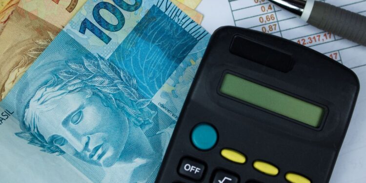 Cédulas de R$ 50 e R$ 100 ao lado de calculadora preta sobre planilha financeira, em referência à renegociação de dívidas pelo Novo Desenrola Brasil
