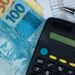 Cédulas de R$ 50 e R$ 100 ao lado de calculadora preta sobre planilha financeira, em referência à renegociação de dívidas pelo Novo Desenrola Brasil