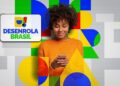 Mulher de blusa laranja sorrindo enquanto utiliza celular ao lado do logotipo do Desenrola Brasil