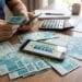 Homem conta cédulas de cem reais ao lado de celular que exibe a marca do Novo Desenrola Brasil e uma calculadora.