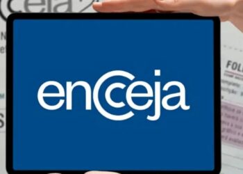 Mãos segurando tablet com logotipo do Encceja em destaque sobre cartão de inscrição e folha de redação