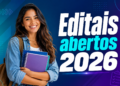 Jovem universitária com cabelos ondulados, camisa jeans e mochila segura cadernos ao lado de texto "Editais abertos 2026".