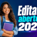 Jovem universitária com cabelos ondulados, camisa jeans e mochila segura cadernos ao lado de texto "Editais abertos 2026".