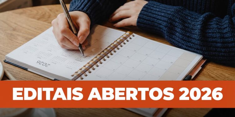 Mãos escrevendo em agenda 2026 com caneta prata sobre mesa de madeira, destacando texto editais abertos 2026