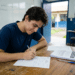 : Estudante preenche ficha de inscrição em sala de aula com cadernos e materiais sobre a mesa