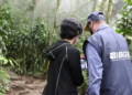 Dois servidores do IBGE com colete e boné institucionais em trabalho de campo dentro de área de mata