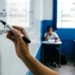 Professor escreve as palavras enquanto e em quanto em quadro branco enquanto estudantes uniformizados acompanham a aula ao fundo