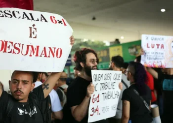 Manifestantes erguendo cartazes com mensagens contra a escala 6x1 durante protesto público