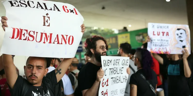 Manifestantes erguendo cartazes com mensagens contra a escala 6x1 durante protesto público