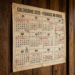 Calendário anual 2026 em papel envelhecido fixado em parede de madeira escura, destacando feriados nacionais do Brasil.