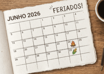 Calendário de junho 2026 sobre mesa de madeira com fogueira no dia 24 e milho no dia 29, xícara de café e caneta.