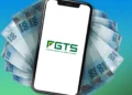 Celular com logo do FGTS sobre notas de R$ 100, representando o uso do fundo para quitar dívidas.
