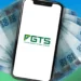 Celular com logo do FGTS sobre notas de R$ 100, representando o uso do fundo para quitar dívidas.