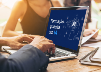 Mãos masculinas digitam em laptop prateado exibindo tela azul com texto "Formação gratuita em IA" e ícone AI.