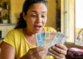 Mulher brasileira surpresa segurando notas de reais, representando o pagamento único de R$ 50 mil liberado pelo Governo do Brasil.