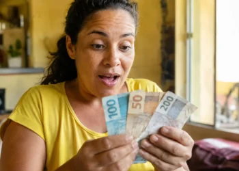 Mulher brasileira surpresa segurando notas de reais, representando o pagamento único de R$ 50 mil liberado pelo Governo do Brasil.