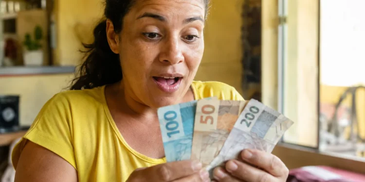 Mulher brasileira surpresa segurando notas de reais, representando o pagamento único de R$ 50 mil liberado pelo Governo do Brasil.