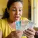 Mulher brasileira surpresa segurando notas de reais, representando o pagamento único de R$ 50 mil liberado pelo Governo do Brasil.
