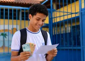 Estudante da rede pública segurando documentos do Enem 2026 e cédulas de dinheiro, representando a gratuidade do exame e o bônus de R$ 200.