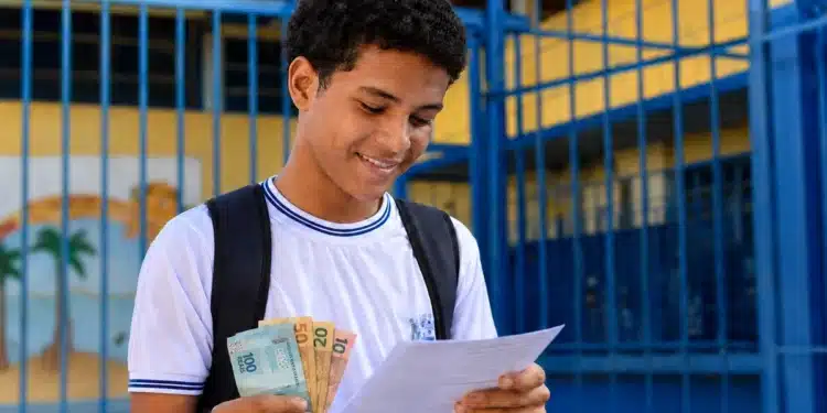 Estudante da rede pública segurando documentos do Enem 2026 e cédulas de dinheiro, representando a gratuidade do exame e o bônus de R$ 200.