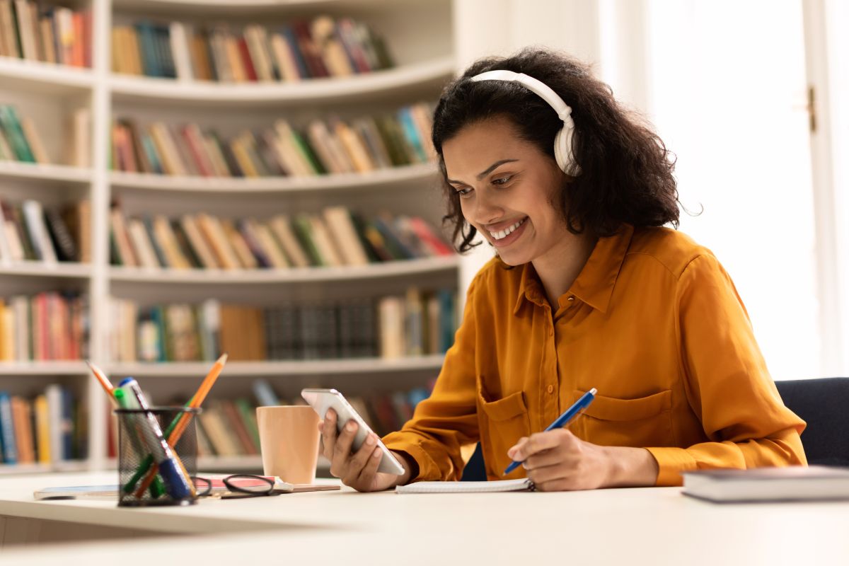 Pessoa estudando idiomas com celular e caderno, representando o aprendizado facilitado para falantes de português.