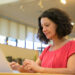 Mulher de blusa vermelha digita em notebook prateado sentada em ambiente de biblioteca com estantes de livros ao fundo