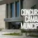 Fachada moderna do prédio da Câmara Municipal com bandeira do Brasil e arte com o texto "Concurso Câmara Municipal".