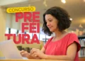 Mulher concentrada estudando em notebook em ambiente de biblioteca, ao lado da inscrição Concurso Prefeitura