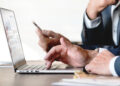 Empresário utilizando notebook e celular para consultas digitais em ambiente corporativo