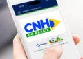 Mão segura um smartphone que exibe a tela inicial do aplicativo CNH do Brasil, plataforma oficial do Ministério dos Transportes e do Serpro para o processo de habilitação no país.