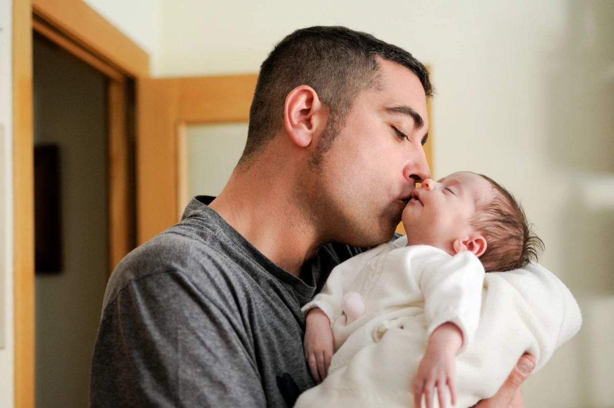 Pai beijando recém-nascido no colo, representando trabalhadores com direito à licença-paternidade e ao salário-paternidade.