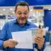 Homem sorrindo, segurando dinheiro e documento em agência bancária, representando pagamento da restituição do Imposto de Renda nesta sexta-feira (29).