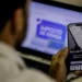 Pessoa acessando serviços da Receita Federal pelo celular enquanto declara o imposto de renda 2026 no computador.