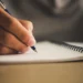 Professor escrevendo anotações em caderno representando a atividade de aperfeiçoamento em matemática