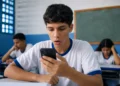 Estudante consultando o celular em sala de aula, representando mensagem do MEC sobre a terceira parcela do programa Pé-de-Meia.