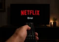Mão segurando controle remoto apontado para TV com aviso de erro da Netflix na tela.
