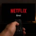 Mão segurando controle remoto apontado para TV com aviso de erro da Netflix na tela.