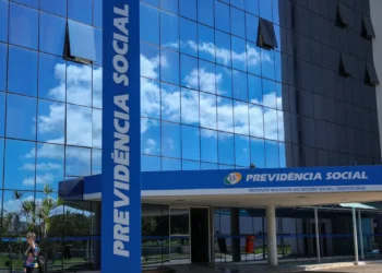 Fachada do edifício sede da Previdência Social com totem azul vertical e céu refletido no vidro espelhado