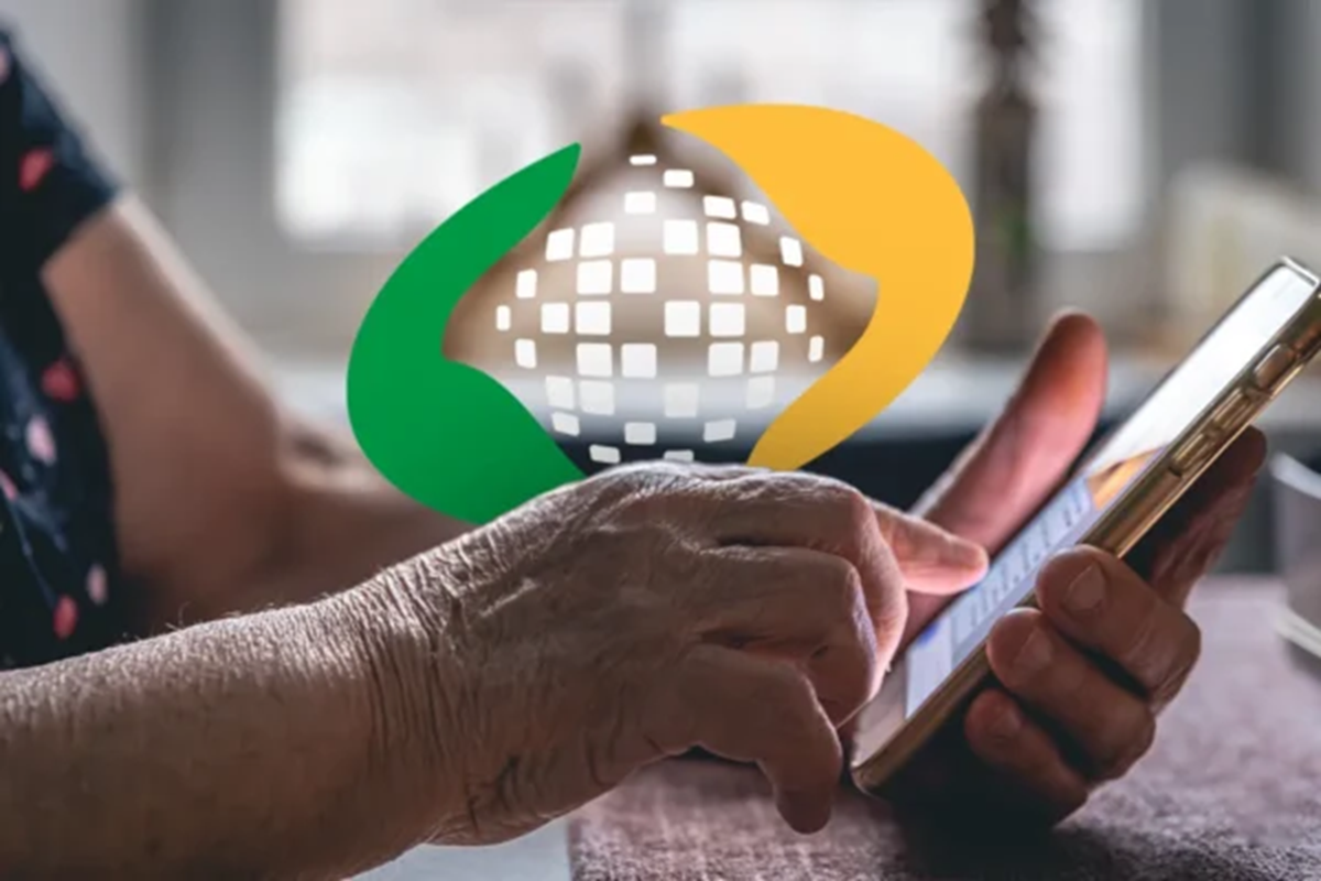 Mãos de pessoa idosa manuseiam celular dourado sobre a mesa com a logomarca do INSS aplicada em destaque sobre a cena