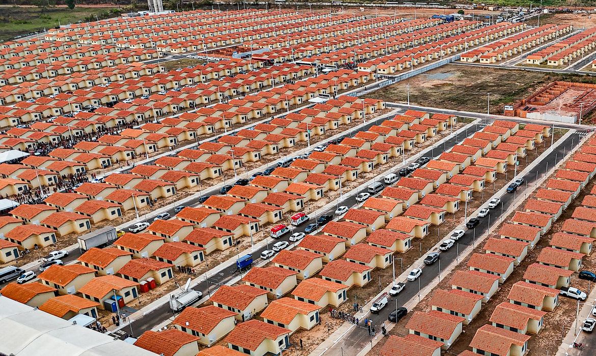 Vista aérea de grande conjunto habitacional com centenas de casas de telhado vermelho enfileiradas, representando as novas unidades do Minha Casa, Minha Vida liberadas em seis estados brasileiros.