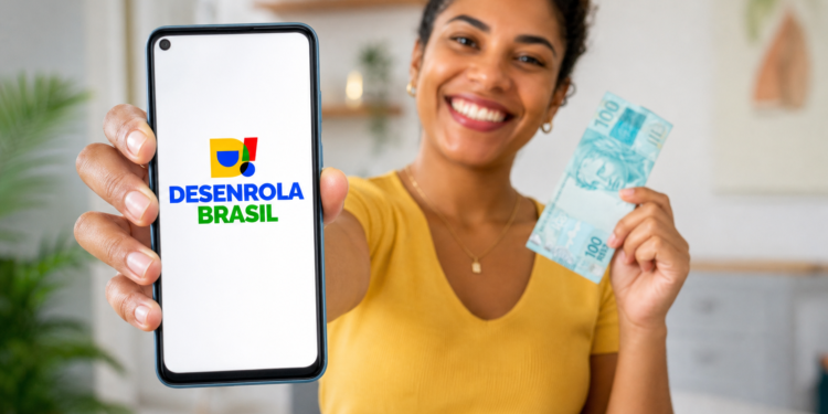 Mulher sorridente exibe smartphone com logo Desenrola Brasil e segura nota de R$ 100 em ambiente doméstico.