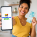 Mulher sorridente exibe smartphone com logo Desenrola Brasil e segura nota de R$ 100 em ambiente doméstico.